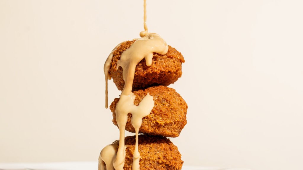 Golden falafel balls stacked and drizzled with creamy tahini sauce on a light background — a classic Middle Eastern food scene for branding and promotional content.