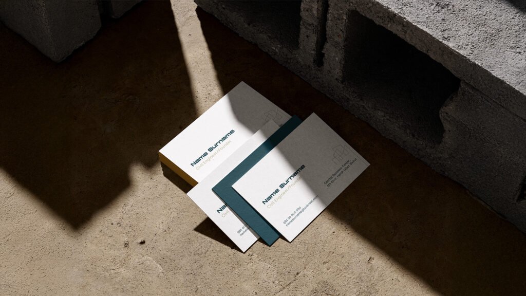 Stack of minimalist business cards for a civil engineer placed on a concrete floor beside cinder blocks, reflecting industrial branding aesthetics.