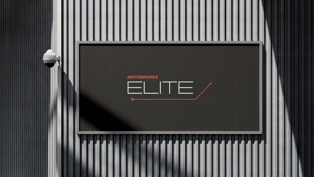 Motorworks ELITE billboard on a modern corrugated metal building facade, featuring minimalist logo design in white and orange.