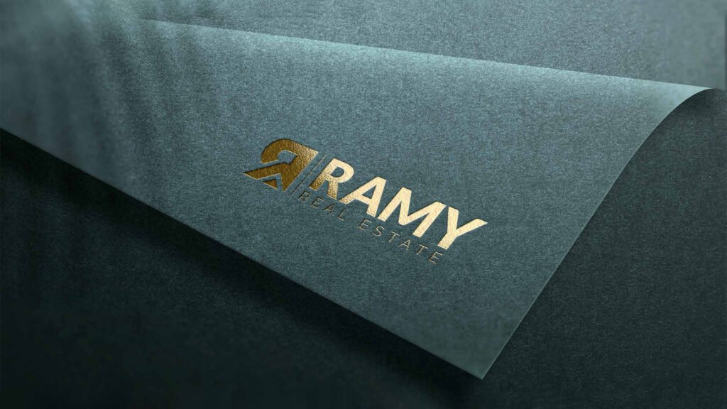 Gold-foil embossed logo for Ramy Real Estate on textured dark green paper, showcasing premium branding design.