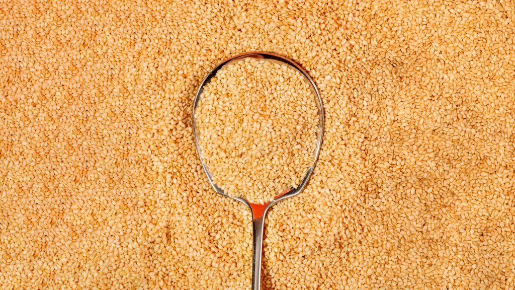 Close-up of golden raw sesame seeds with a metal spoon, perfect for natural ingredient branding and healthy food marketing.