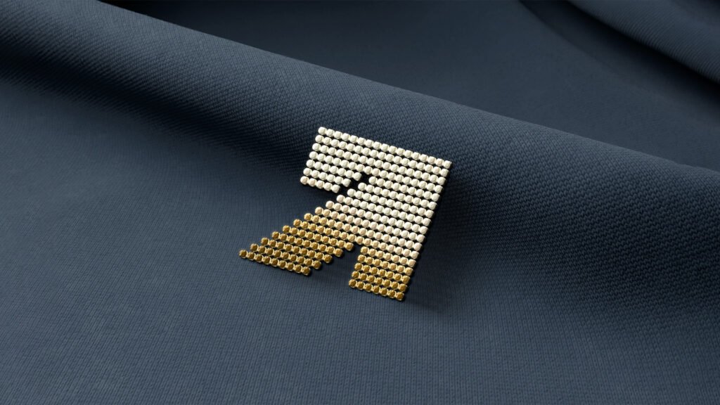 Gold and silver metallic pin in the shape of the Armada Solutions logo placed on dark blue fabric.