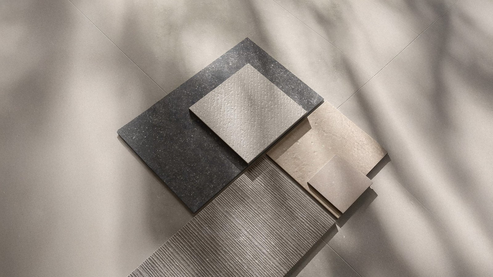 Assorted textured ceramic and stone tile samples laid on a neutral-toned floor in natural lighting.