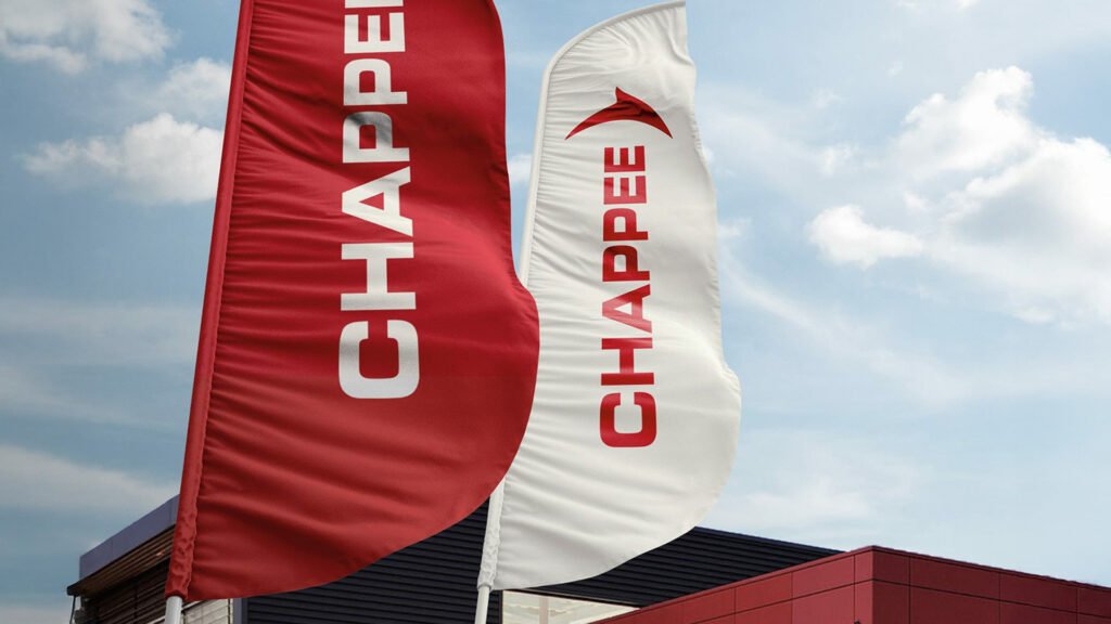Two outdoor Chappée flags — one red, one white — flying side by side in front of a modern red building under a blue sky.