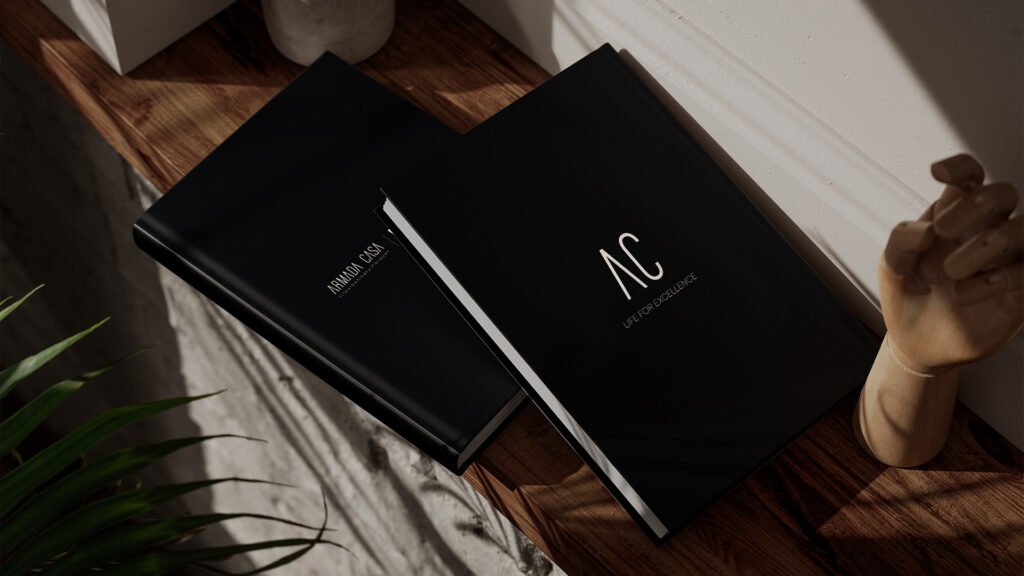 Two elegant black catalogs on a wooden shelf, featuring the Armada Casa and AC "Life for Excellence" branding.