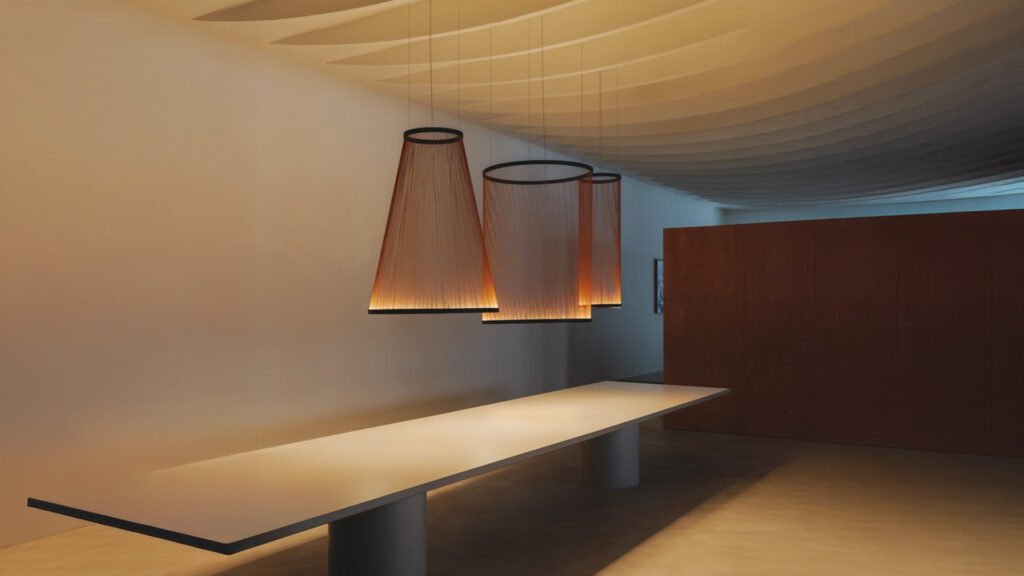 Contemporary pendant lighting installation above a minimalist table in a softly lit interior with sculpted ceiling design.