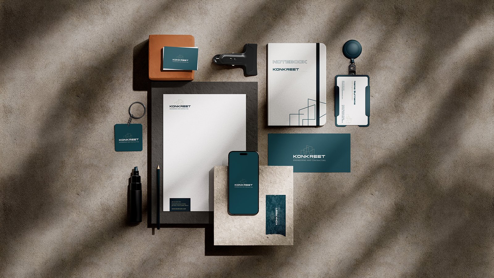Flat-lay display of Konkrete Engineering and Contracting branded stationery set including notebooks, business cards, ID tags, phone, and keychain on a textured surface.
